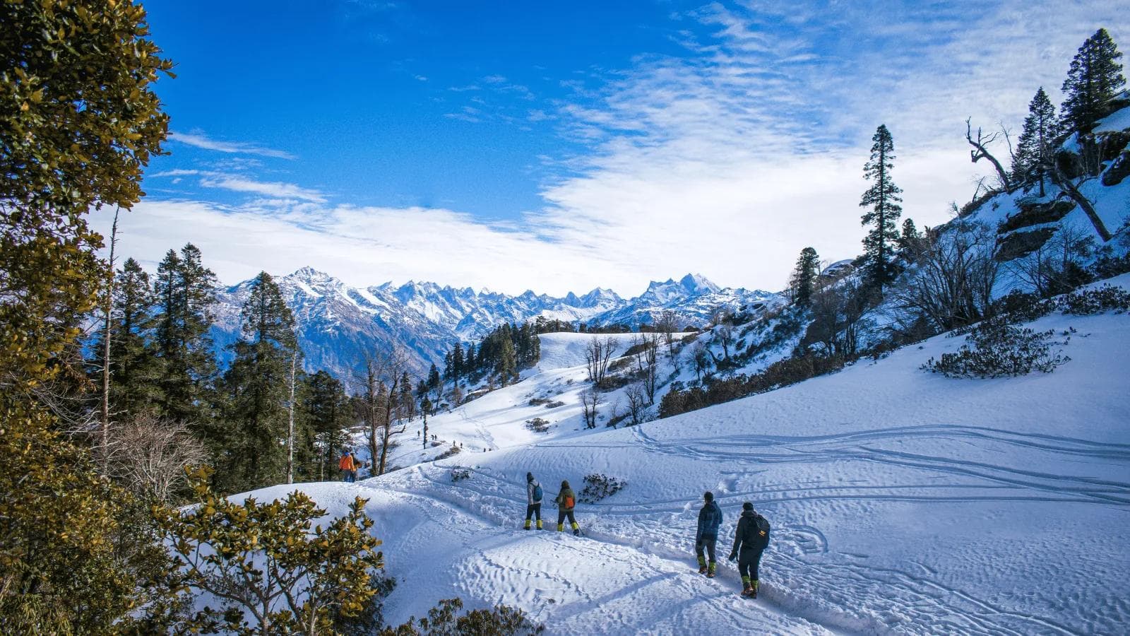Snowy Kedarkantha landscape with trekkers, pine forest and Himalayan peaks